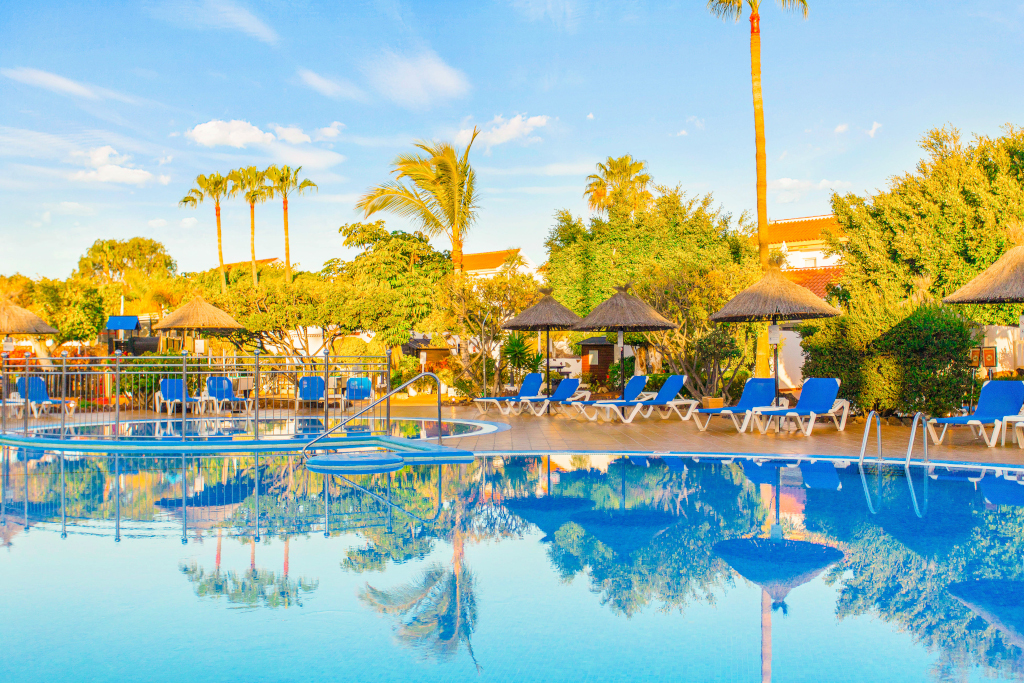 Piscina con tumbonas y palmeras en Tenerife reflejada en el agua.