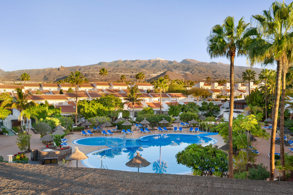 Complejo turístico en Tenerife con piscina y montañas al fondo.