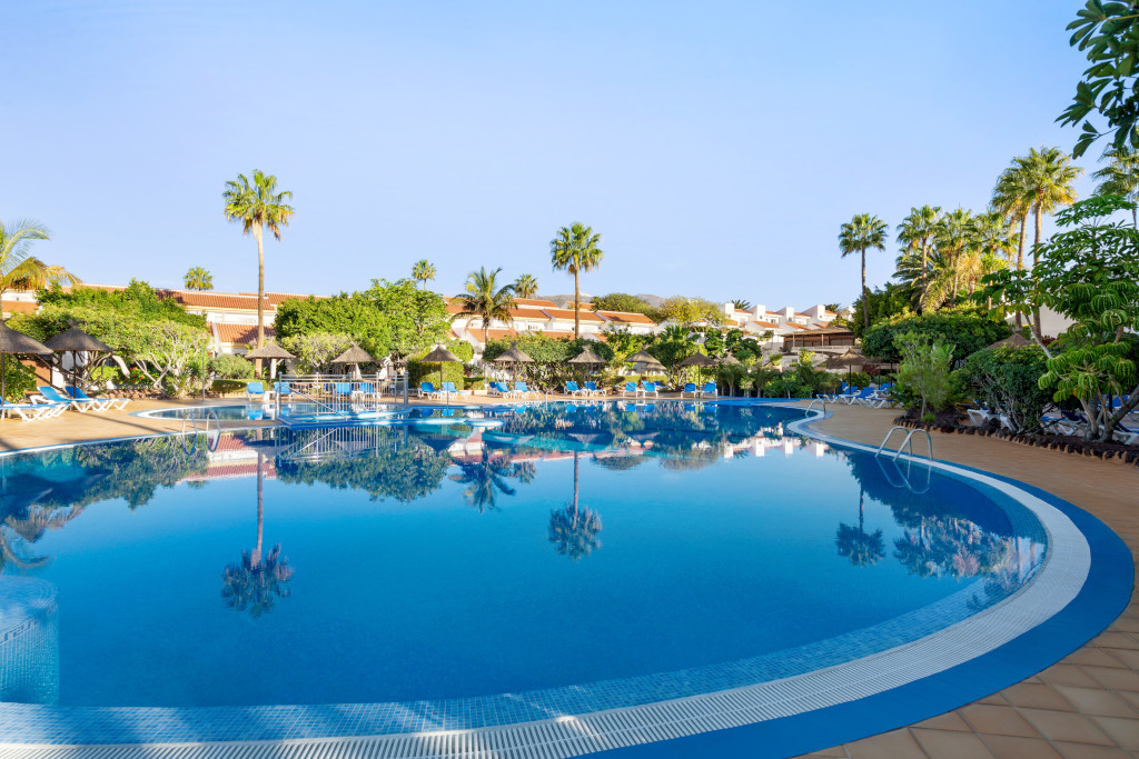 Piscina rodeada de palmeras y tumbonas en un hotel de Tenerife.
