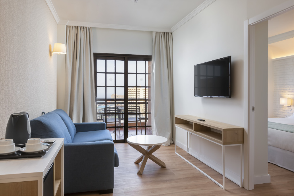 Sala de estar de hotel en Tenerife con sofá azul y televisor montado en la pared.