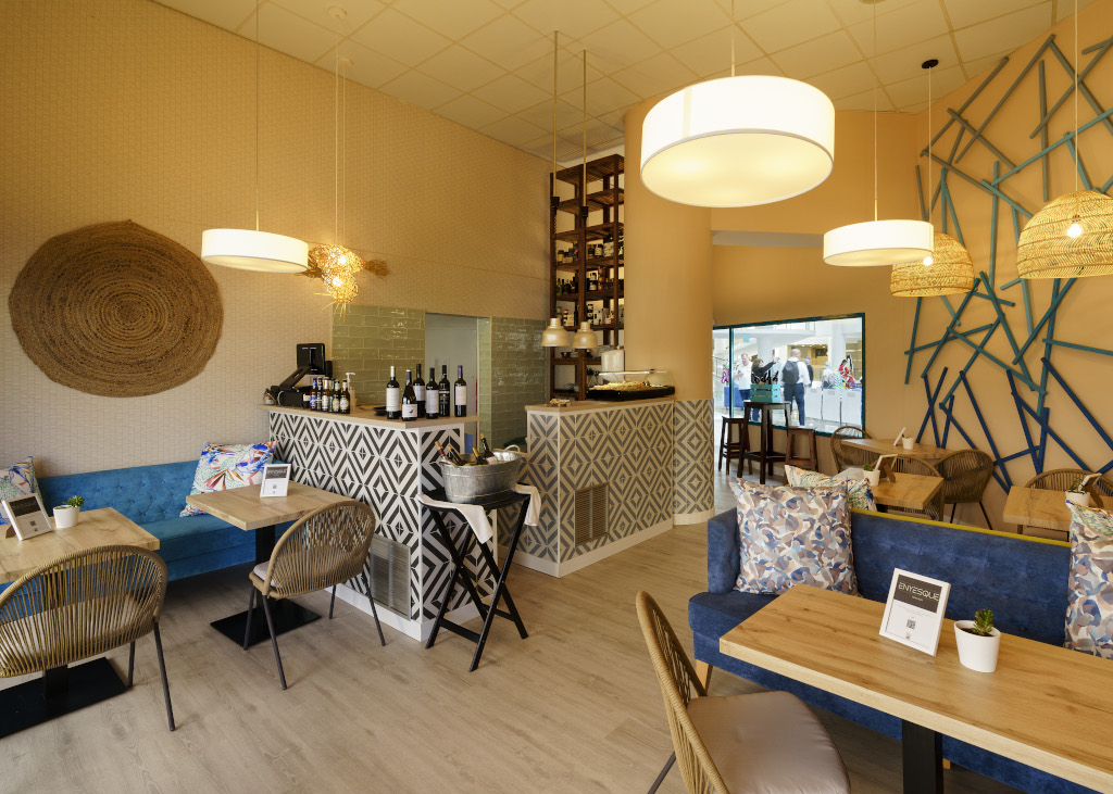 Interior de cafetería en Tenerife con mesas de madera, sillas de mimbre y botellas de vino.