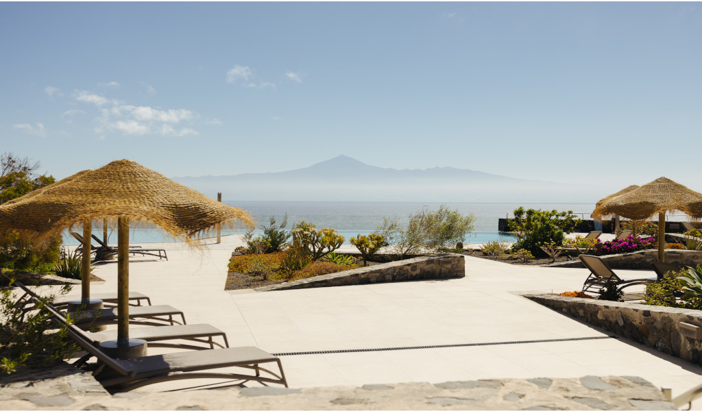 Terraza con sombrillas y tumbonas en Tenerife, vista del mar y montaña al fondo.