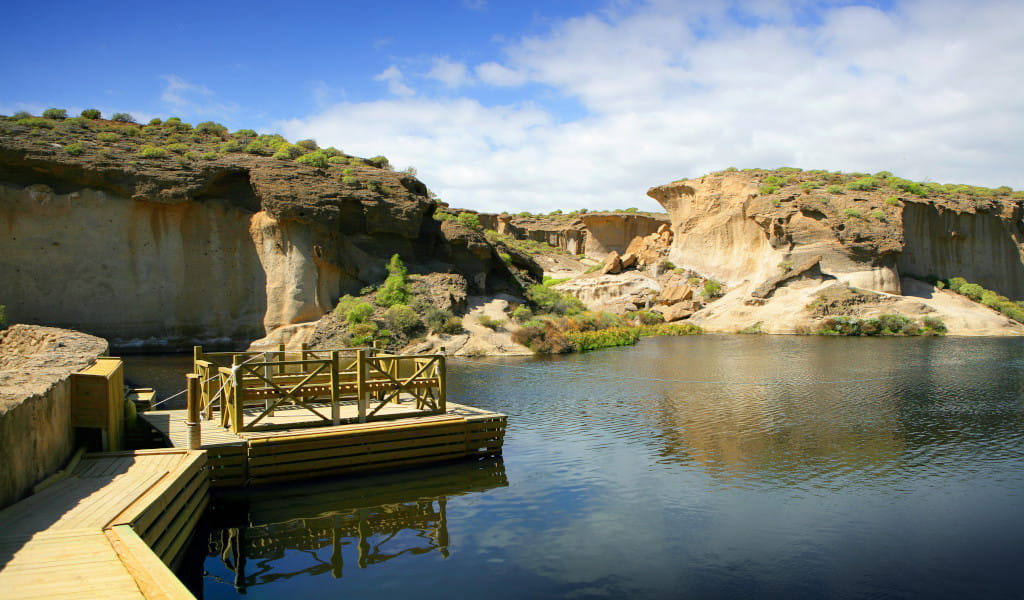 Pasarela de madera sobre un lago con formaciones rocosas en Tenerife.