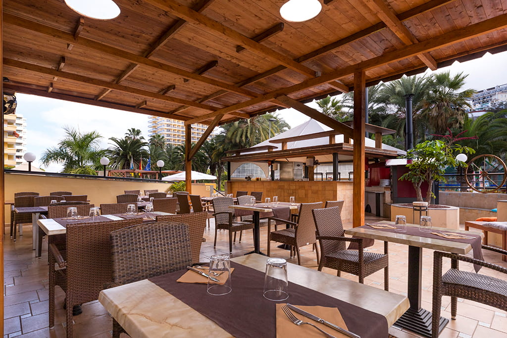 Terraza con mesas y sillas de mimbre bajo pérgola en restaurante de Tenerife.