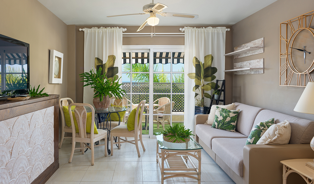 Sala de estar con sofá, mesa de vidrio y plantas junto a ventana en Tenerife.