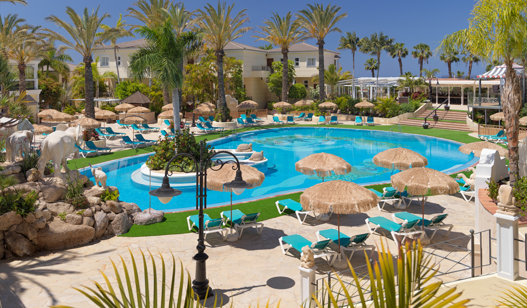 Piscina rodeada de palmeras y tumbonas en un hotel en Tenerife.
