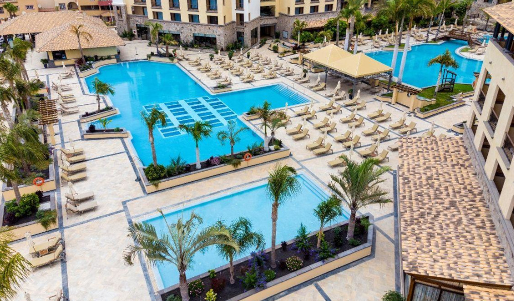 Complejo de piscinas y tumbonas en hotel de Tenerife, rodeado de palmeras.