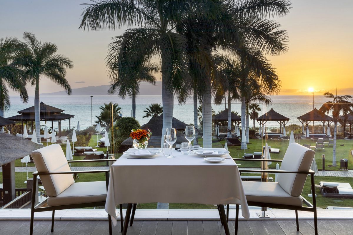 Mesa con vista al atardecer en la playa de Tenerife, rodeada de palmeras.