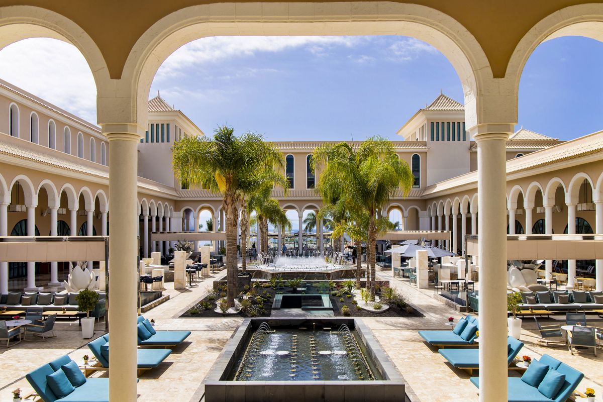 Patio del hotel en Tenerife con piscina, palmeras y tumbonas.