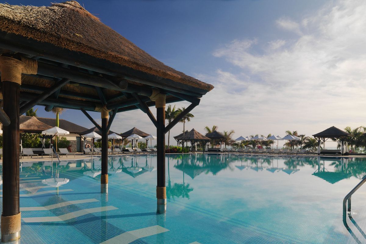 Piscina al aire libre con palapas y tumbonas en un resort en Tenerife.