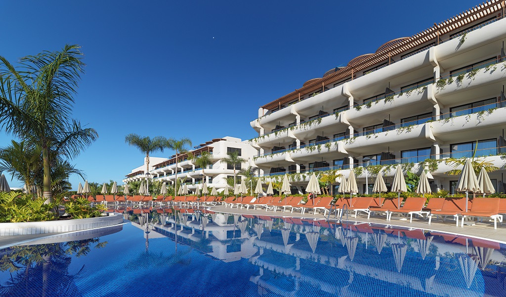 Piscina con sombrillas y hotel en Tenerife bajo cielo despejado.