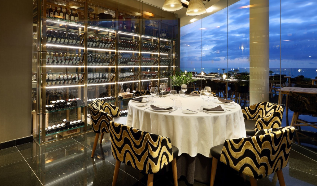 Mesa redonda con copas en un restaurante elegante en Tenerife, junto a un estante de vinos.