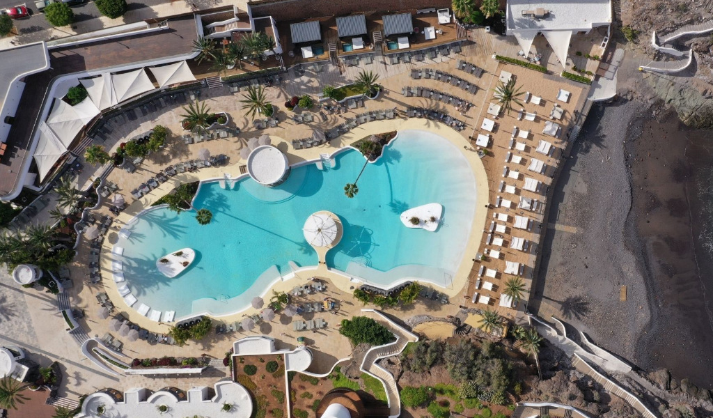 Piscina exterior junto a la playa en Tenerife, rodeada de tumbonas y palmeras.