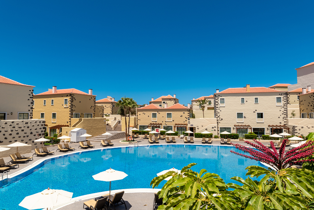 Edificios alrededor de una piscina en un hotel en Tenerife bajo cielo azul.