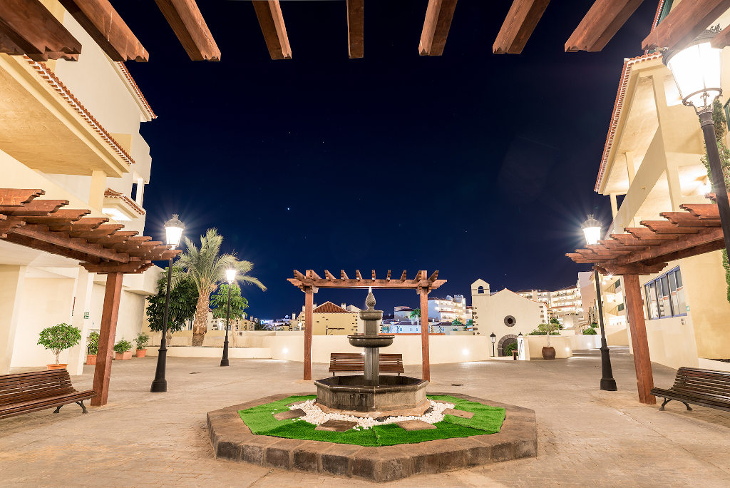 Plaza iluminada en la noche con fuente y bancos, en Arona, Tenerife.
