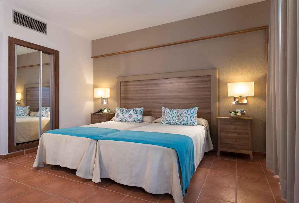 Cama doble en habitación con espejo y lámparas en Tenerife.