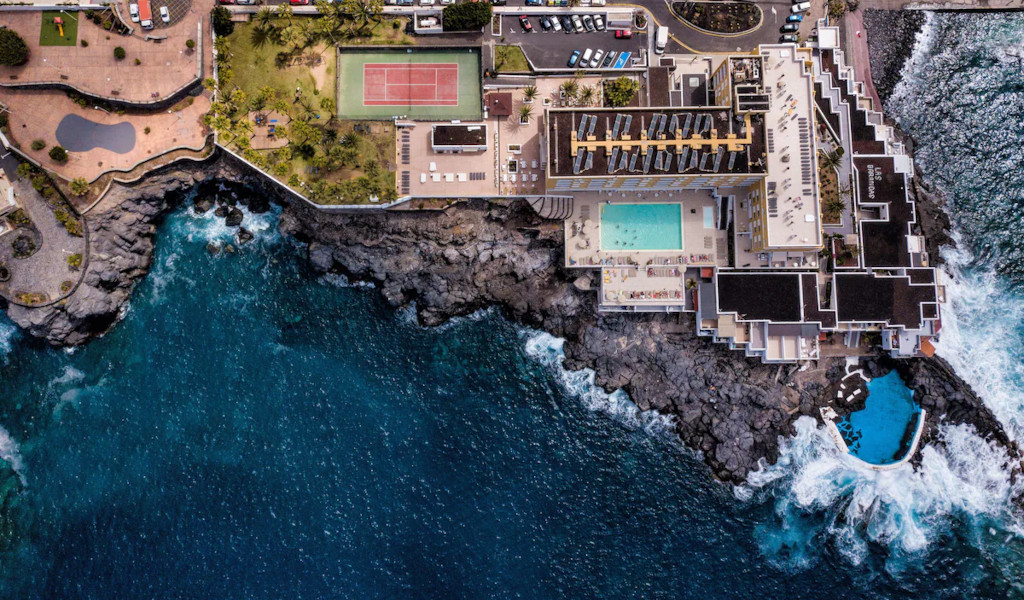 Vista aérea de un hotel junto al mar en Tenerife, con piscina y cancha de tenis.