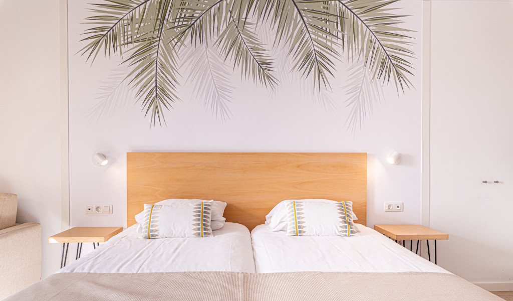 Cama doble con cabecero de madera y estampado de hojas en la pared en Tenerife.