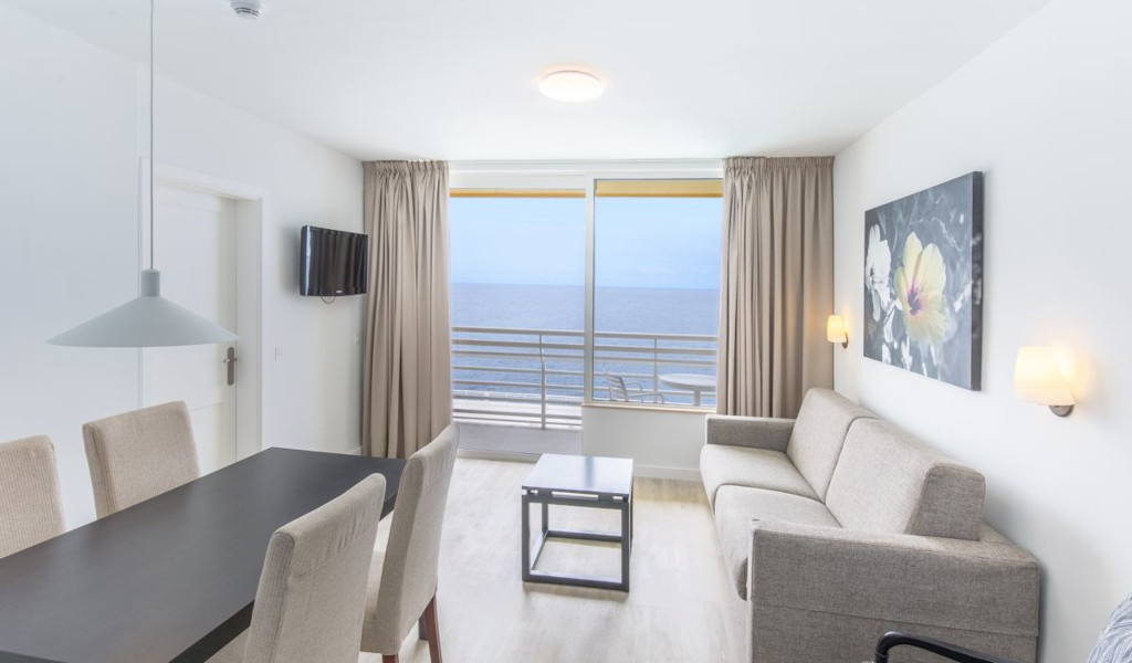 Sala de estar en Tenerife con mesa, sofá, televisor y vista al mar.