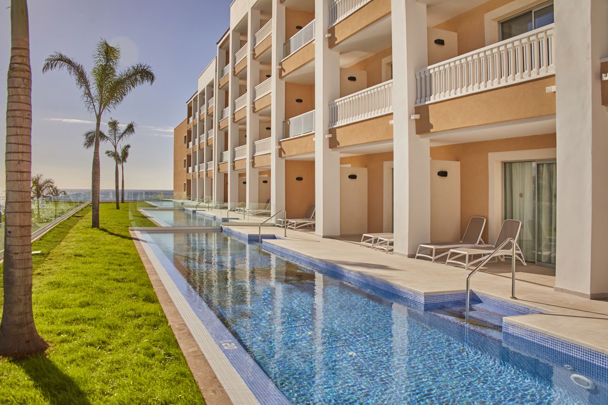 Hotel con piscina y palmeras en Tenerife con vista al océano.