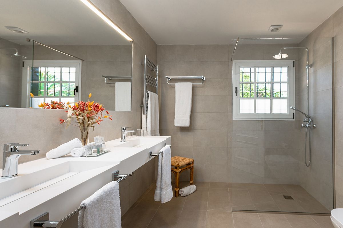 Baño moderno con ducha y lavabo en Tenerife, toallas y ventana grande.