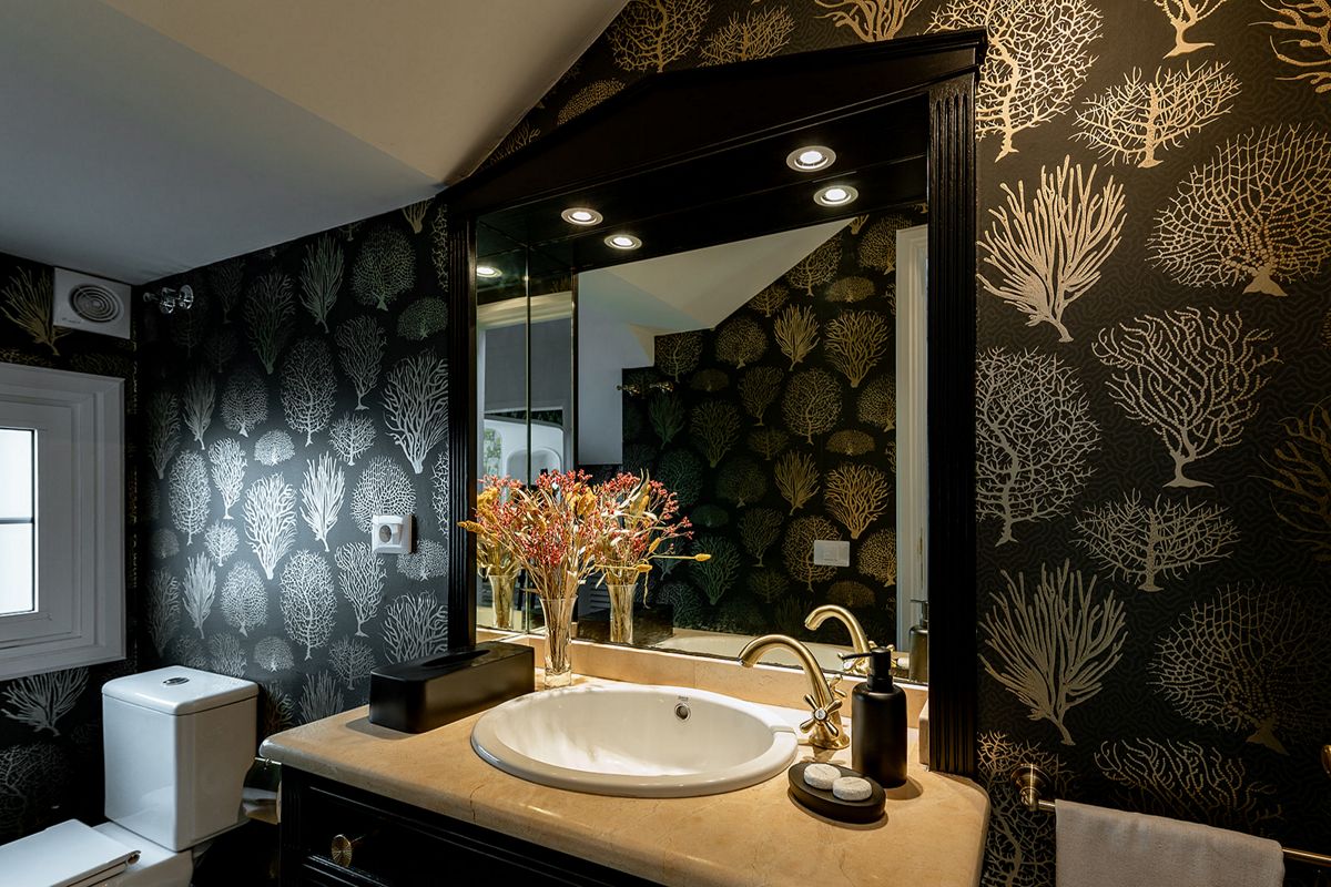 Baño elegante con lavamanos, espejo amplio y papel tapiz de corales en Tenerife.