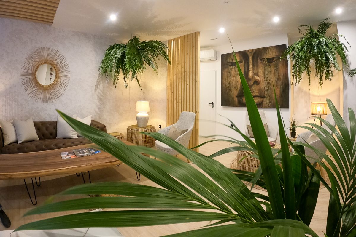 Sala de espera decorada con plantas, sofá marrón y espejo redondo en Tenerife.