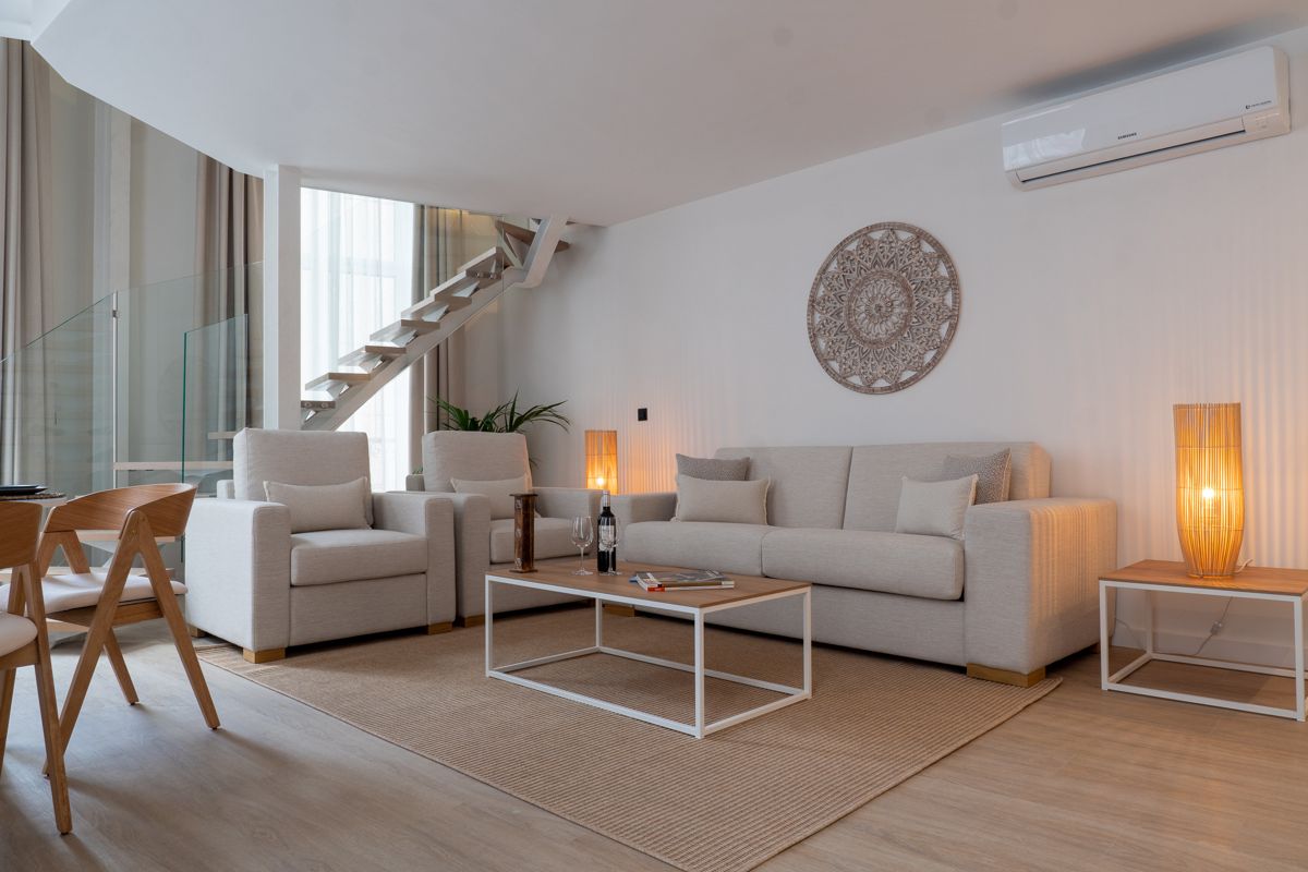 Sala de estar moderna con sofás beige y escalera en Tenerife.