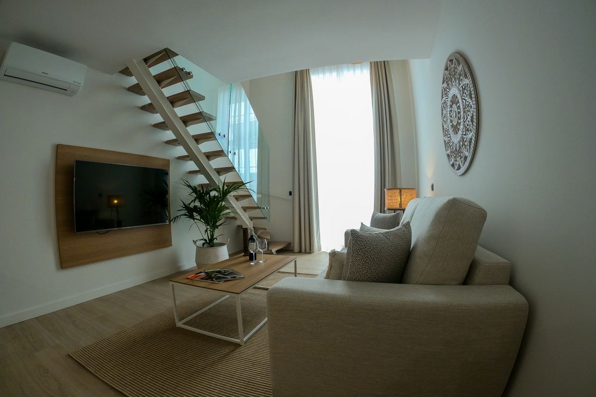 Sala moderna en Tenerife con sofá, escalera y televisión en la pared.