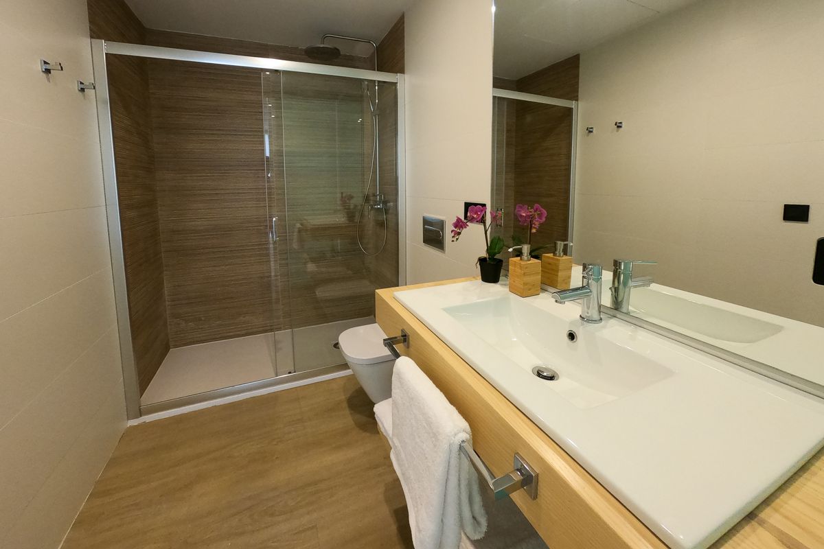 Baño moderno con ducha, lavabo y orquídeas en un apartamento de Tenerife.