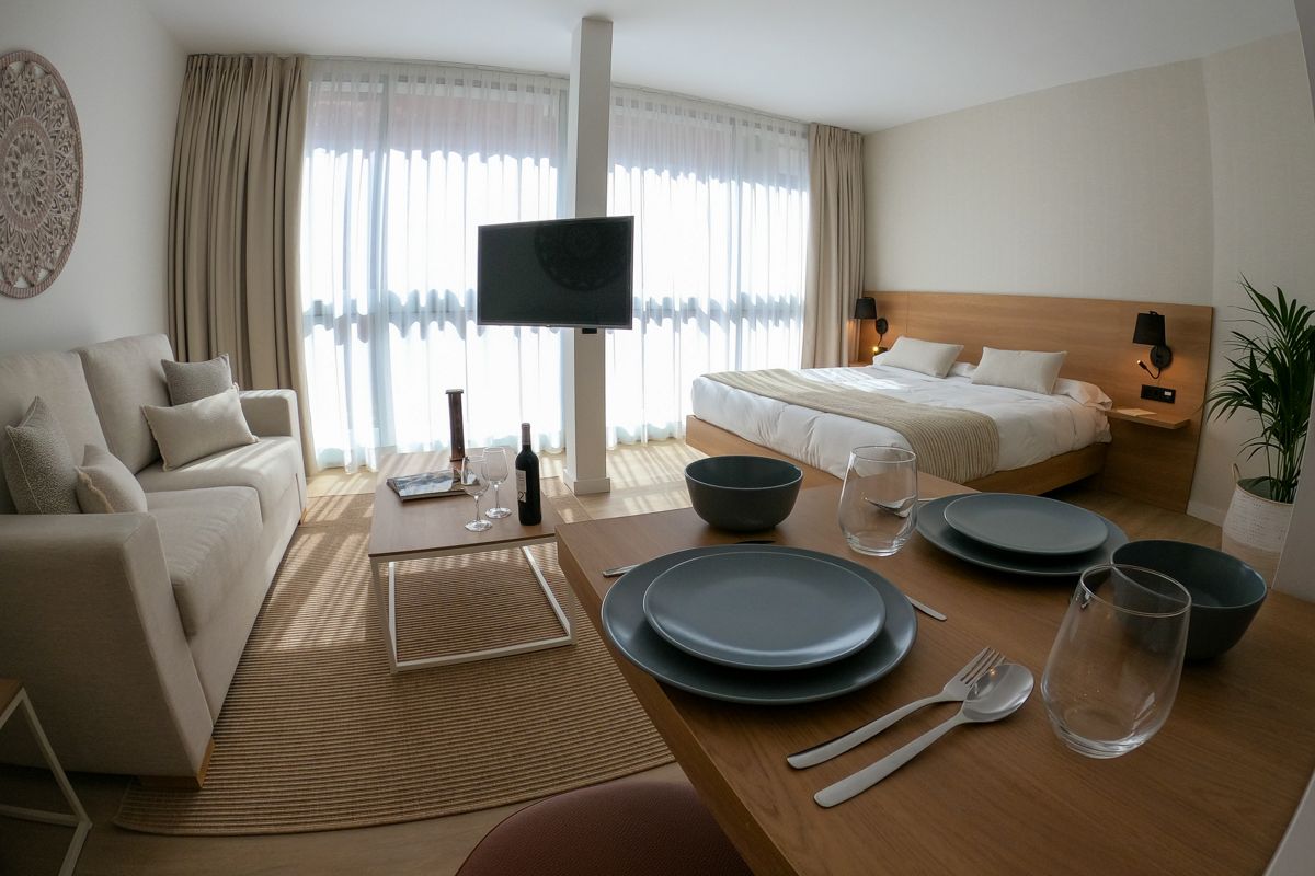 Habitación en Tenerife con cama, sofá y mesa de comedor preparada para dos.