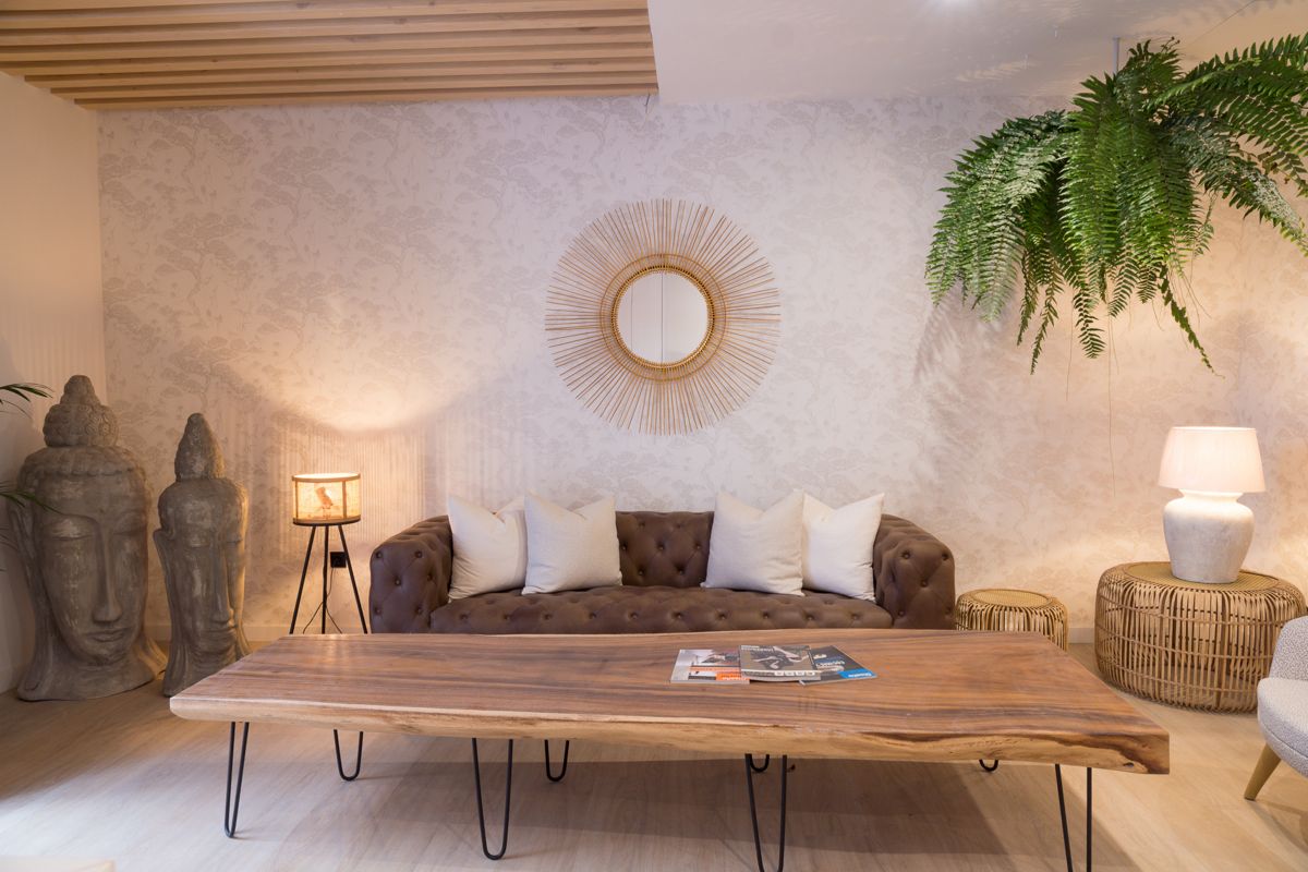Sala de estar en Tenerife con sofá, mesa de madera, figuras de Buda y planta colgante.