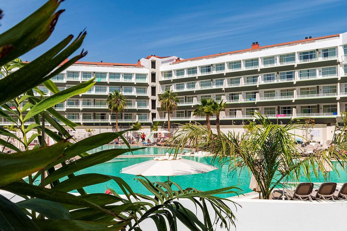 Piscina y hotel con balcones y palmeras en Tenerife.