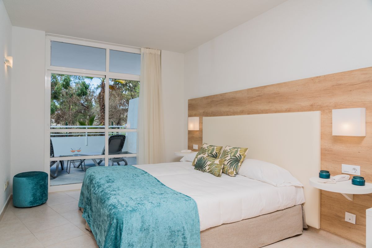 Dormitorio con cama doble, cojines verdes, ventana y terraza con sillas en Tenerife.