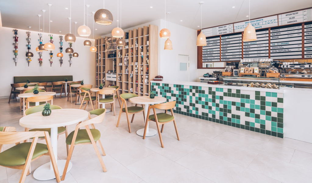 Cafetería moderna en Tenerife con sillas de madera y mostrador con azulejos verdes.