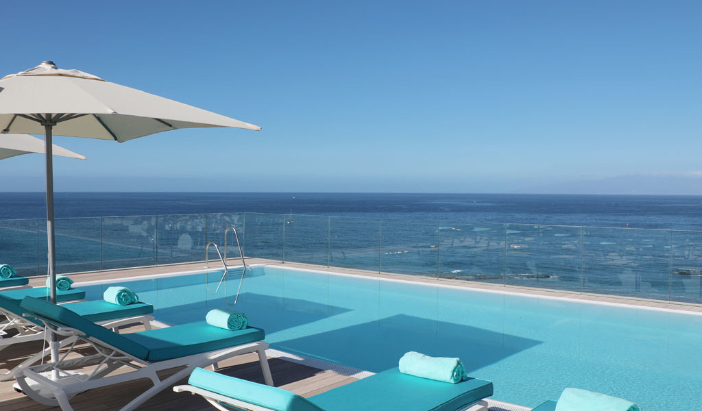 Piscina con vistas al mar en Tenerife, con tumbonas y sombrillas al lado.