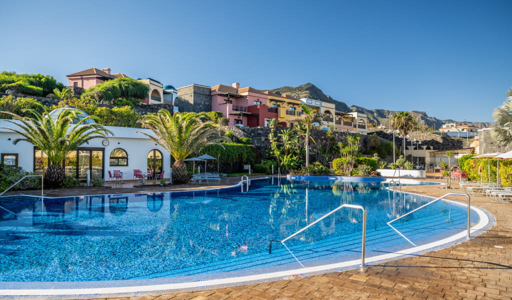 Piscina rodeada de palmeras y edificios en Tenerife bajo cielo despejado.