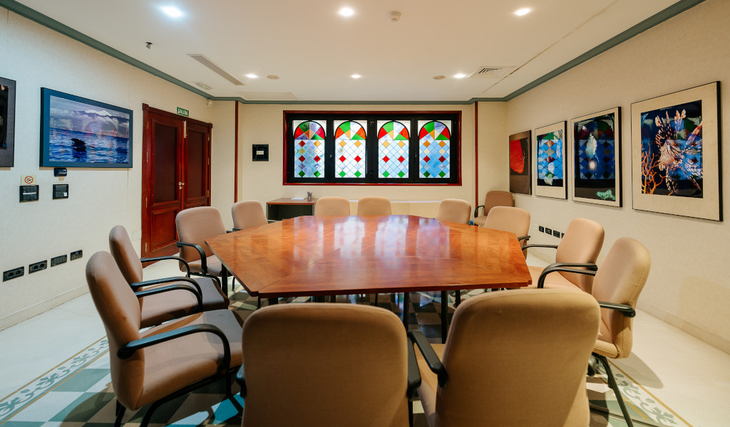 Sala de reuniones con mesa de madera, sillas beige y vidrieras coloridas en Tenerife.