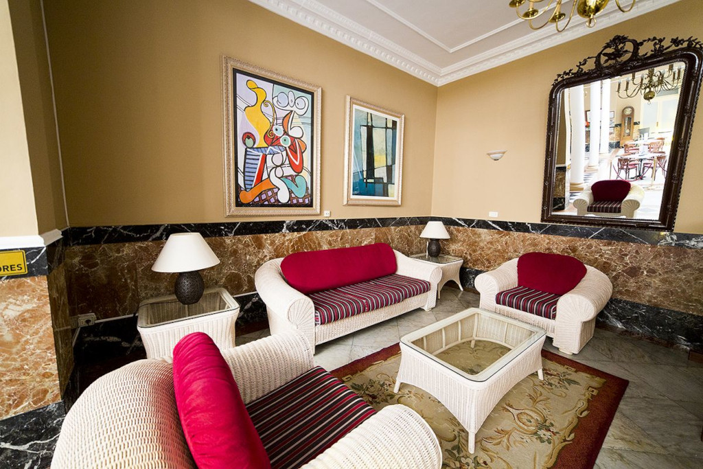 Salón con sofás rojos y mesas junto a un espejo grande en un hotel de Tenerife.