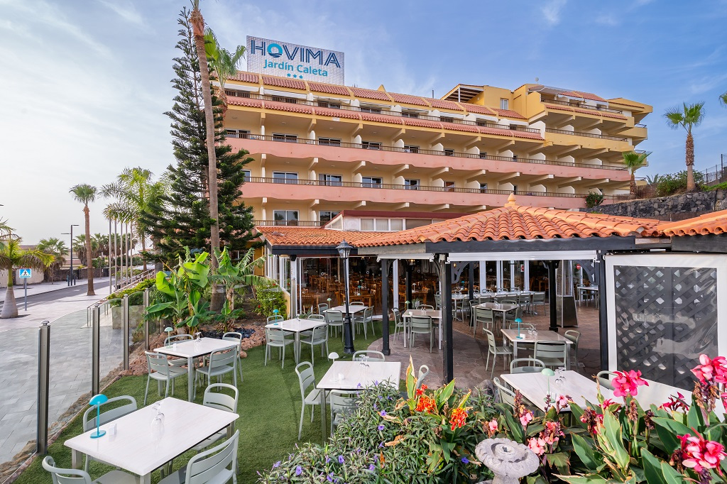 Terraza del hotel Hovima Jardín Caleta en Tenerife, con mesas al aire libre y vegetación.