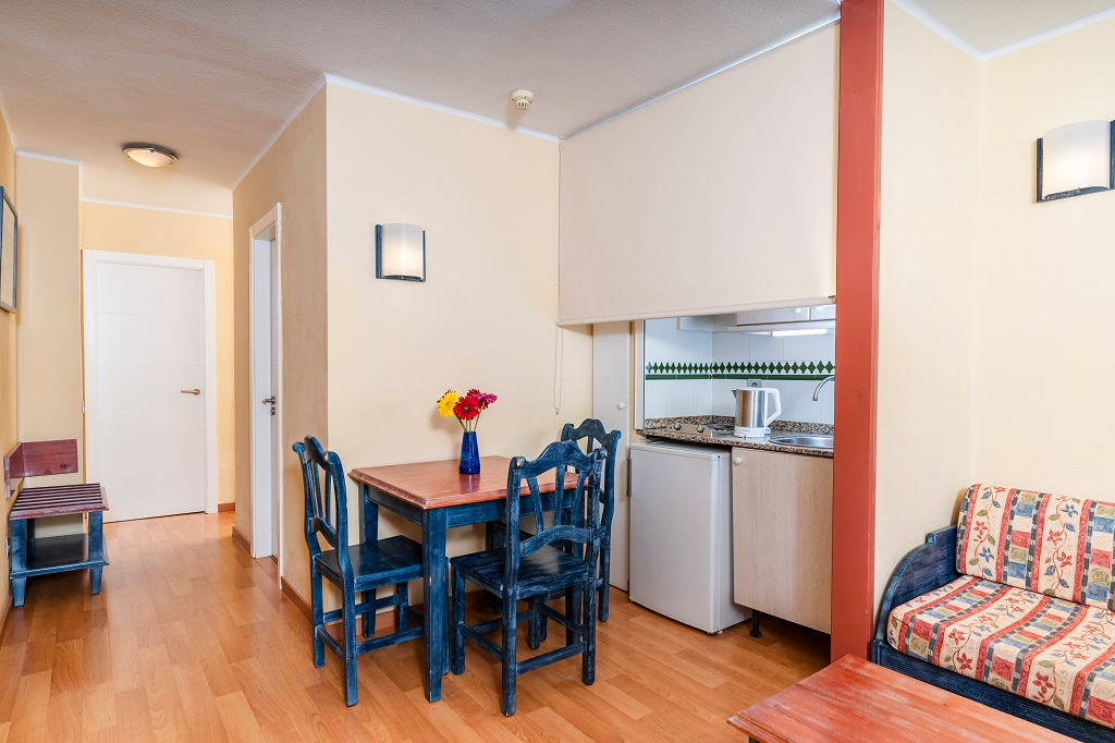 Comedor con mesa de madera, cocina y sofá en apartamento de Tenerife.