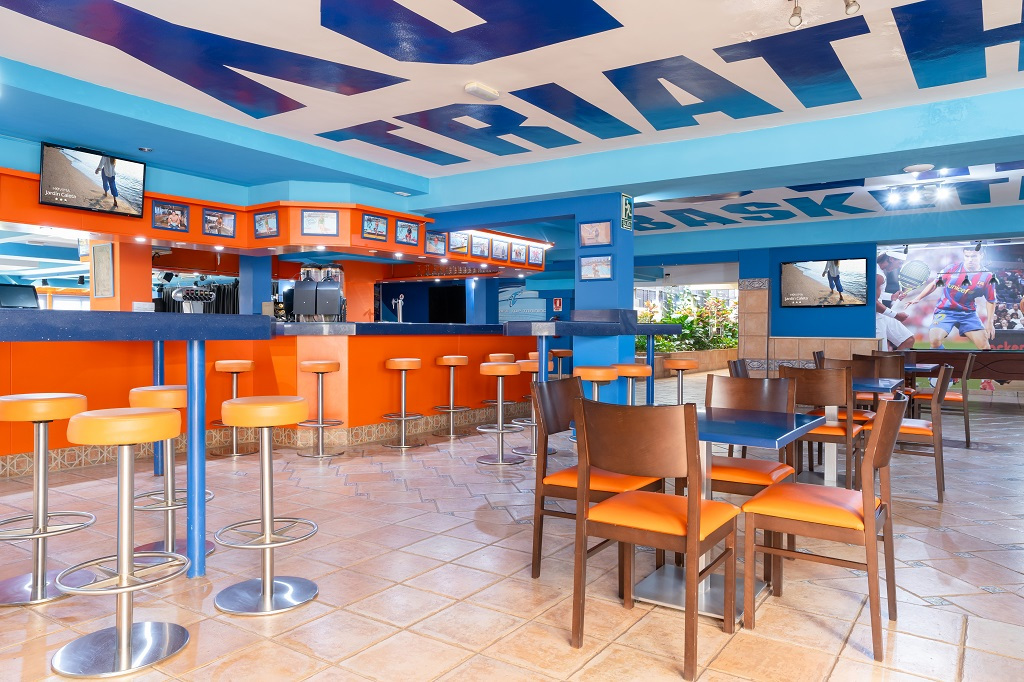 Interior de bar colorido con mesas y sillas en Tenerife, techo decorado con letras grandes.