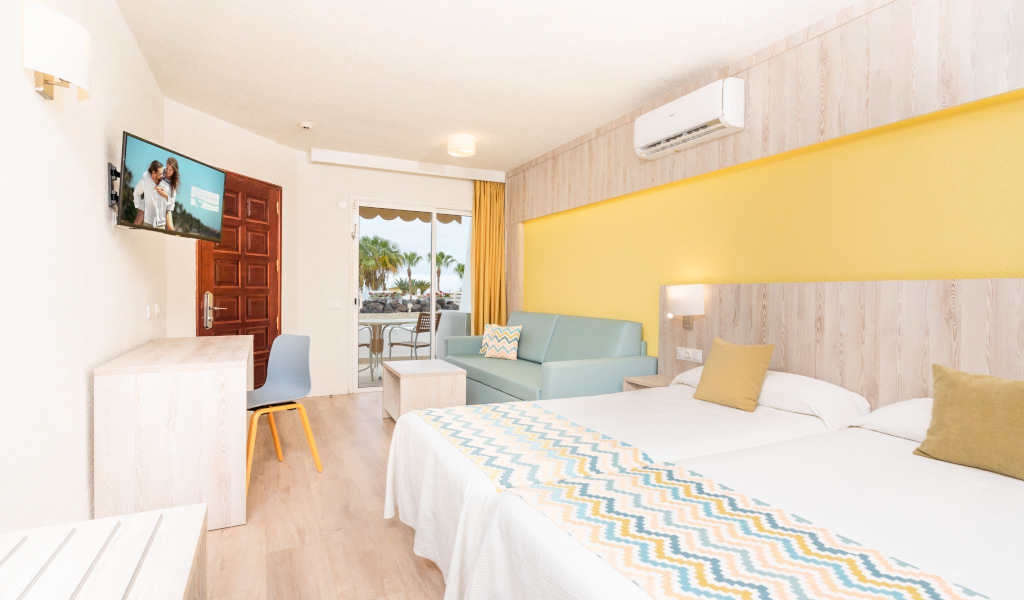 Habitación de hotel en Tenerife con cama doble, sofá y televisión.