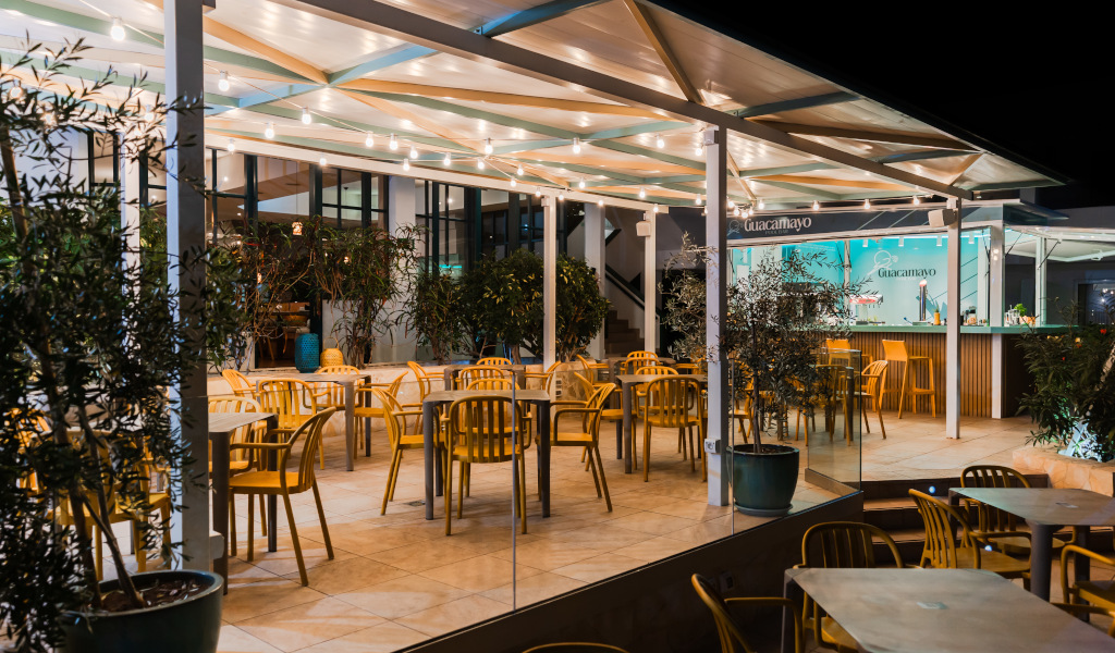 Terraza iluminada del restaurante Guacamayo en Tenerife con mesas y sillas vacías.