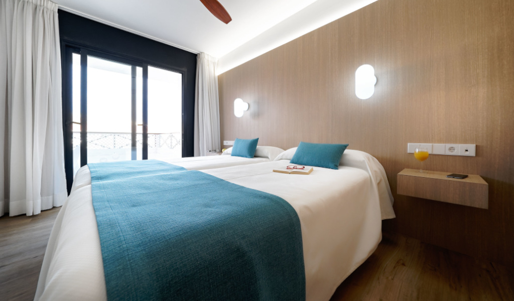 Habitación de hotel en Tenerife con cama doble, sábanas blancas y cojines azules.
