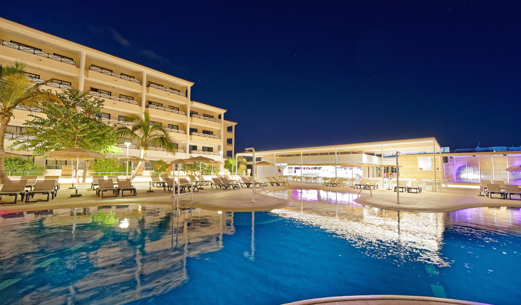 Piscina iluminada frente a hotel de cuatro pisos en Tenerife noche estrellada.