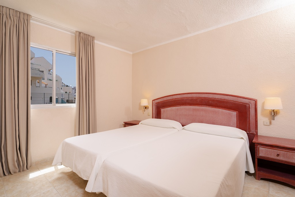 Dos camas individuales en habitación con ventana y lámpara en Tenerife.