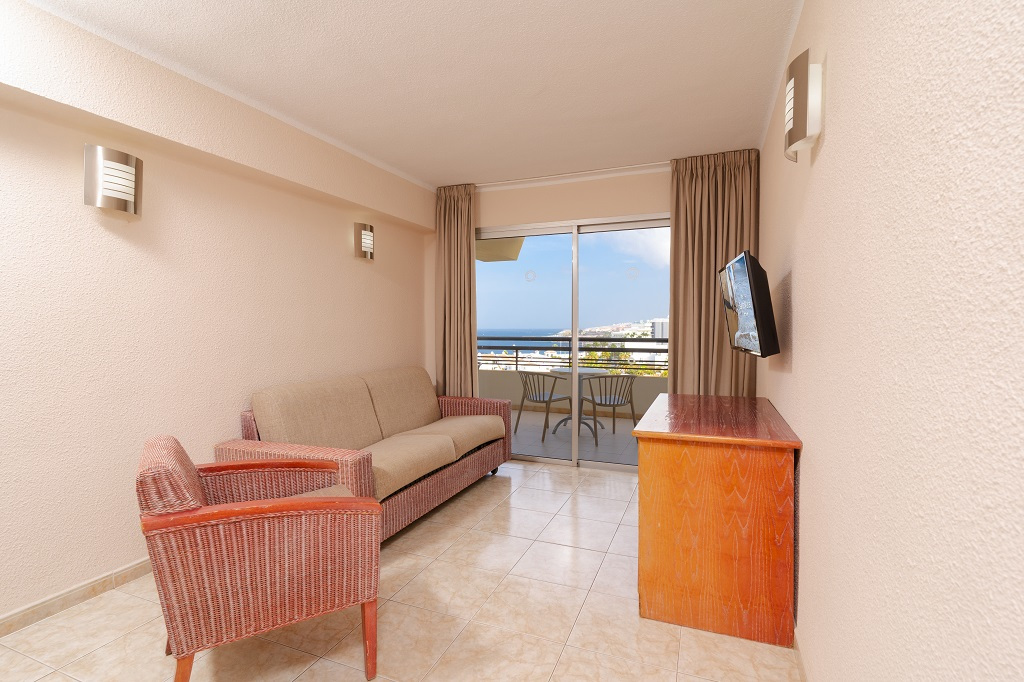 Sala de estar con sofá, televisión y balcón con vista al mar en Tenerife.