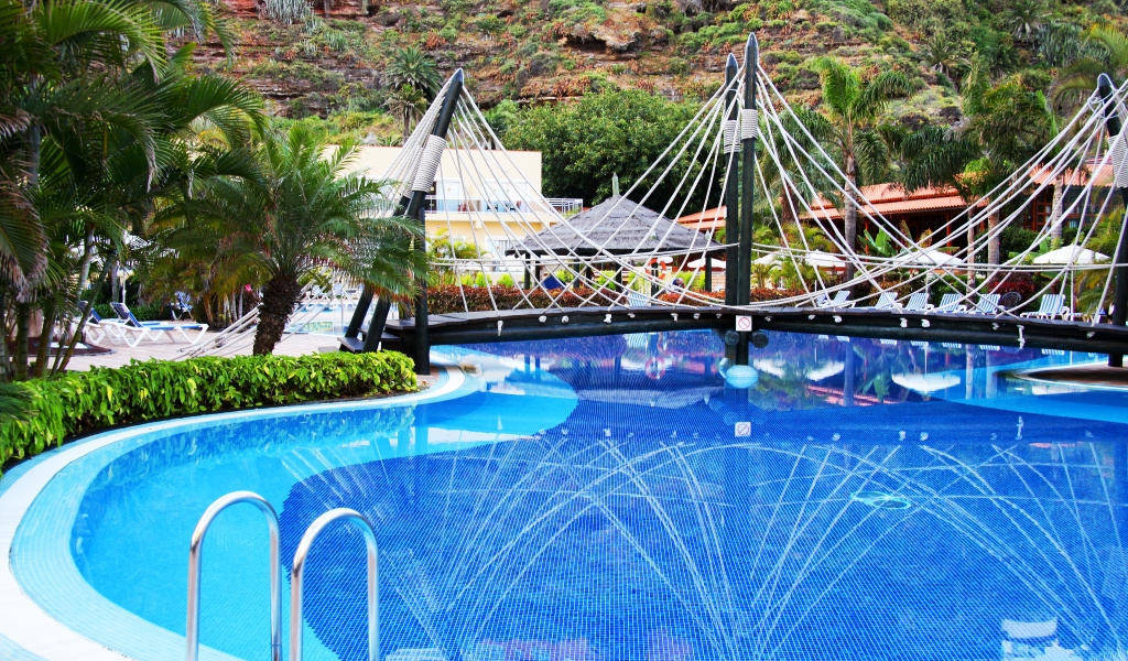 Piscina con puente colgante en un hotel en Tenerife, rodeada de palmeras.