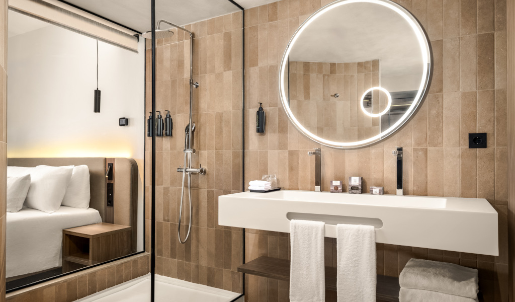 Baño moderno con espejo redondo, ducha y vista parcial de habitación en Tenerife.
